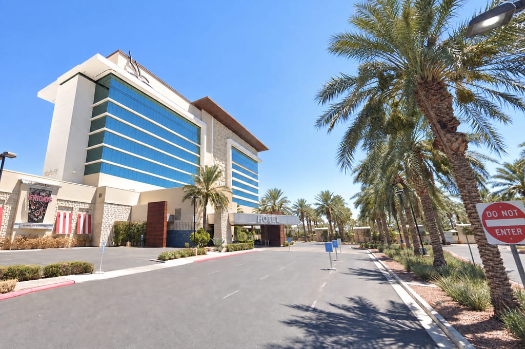 A tall hotel tower banded in blue glass and cream walls, with a HOTEL canopy over the entrance drive and a long row of palms beside the road.