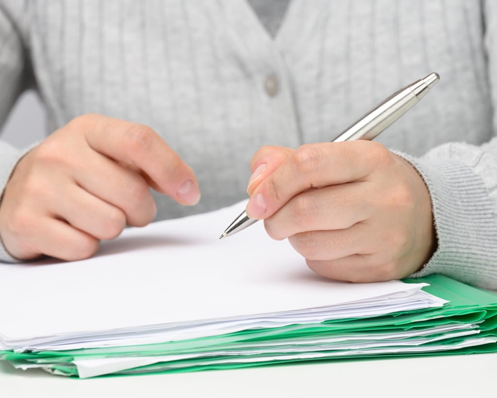 Hands holding a silver pen over a stack of paperwork