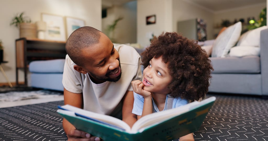 A father and child reading a book together on their living room floor