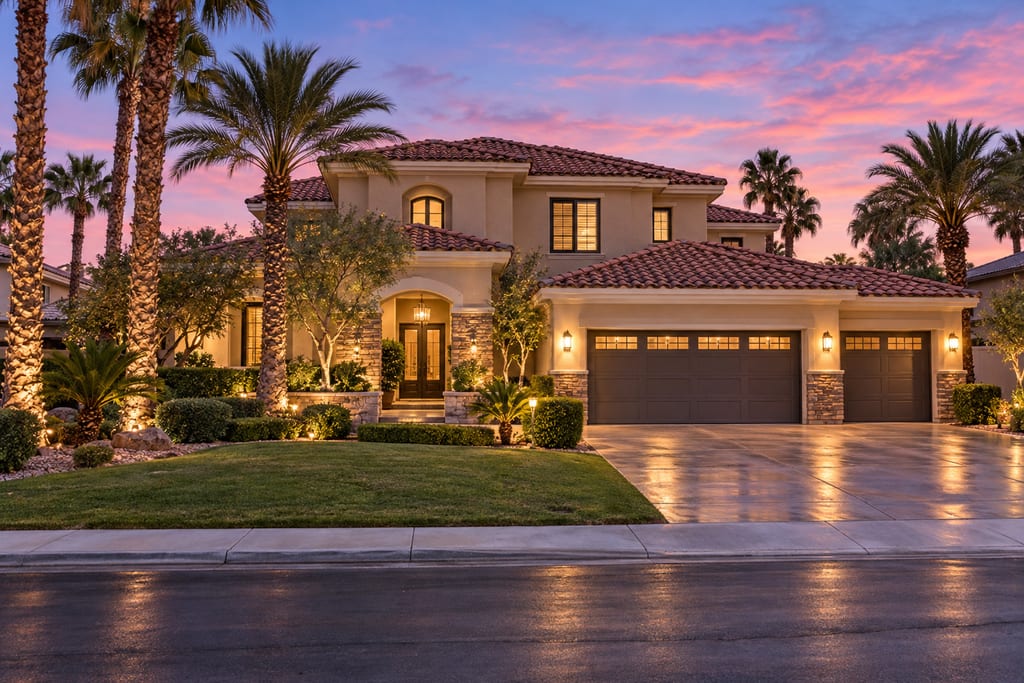 A two-story stucco house with a red tile roof and a three-car garage, lit at dusk under a pink sky