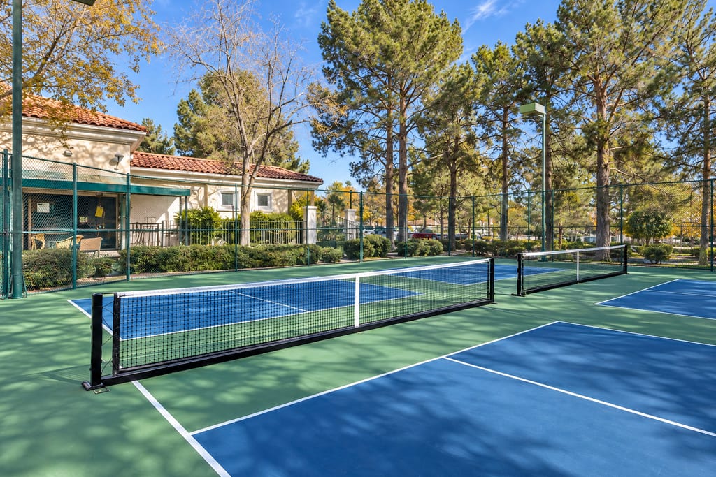 Pickleball courts in dappled shade beside a cream club building with a red tile roof