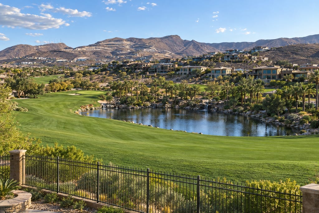 A backyard view over an iron fence down to a golf fairway and a pond, with homes on the hillside and mountains beyond