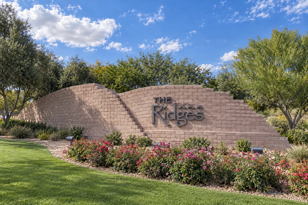 An entrance wall reading “The Ridges” in dark metal letters, above a bed of roses and a lawn