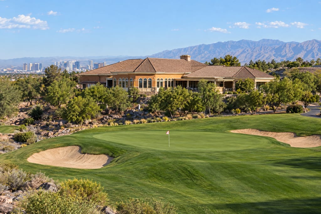 A putting green between two bunkers below a tile-roofed clubhouse, with a city skyline far off on the left