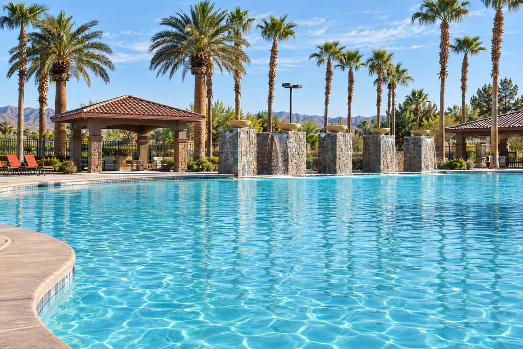 A large curving pool with stone pillars pouring water into it, and palms and a tiled pavilion behind