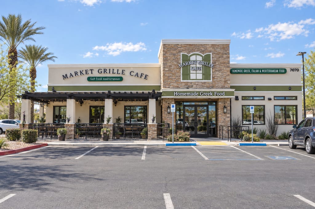 The Market Grille Cafe, a stone and stucco building with a pergola-covered patio, a Homemade Greek Food sign over the doors and the street number 7070, faces an open parking lot.