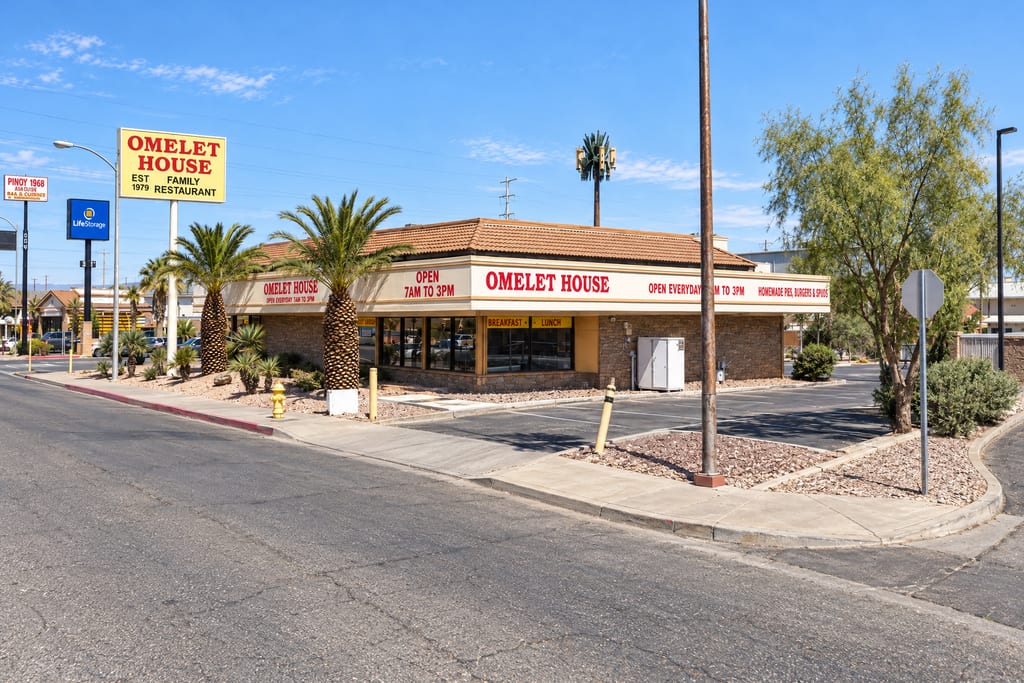 A tile-roofed Omelet House restaurant with red lettering for breakfast and lunch, open 7am to 3pm, sits on a corner lot behind palm trees, and a yellow Omelet House Family Restaurant pole sign reading Est 1979 stands at the street.