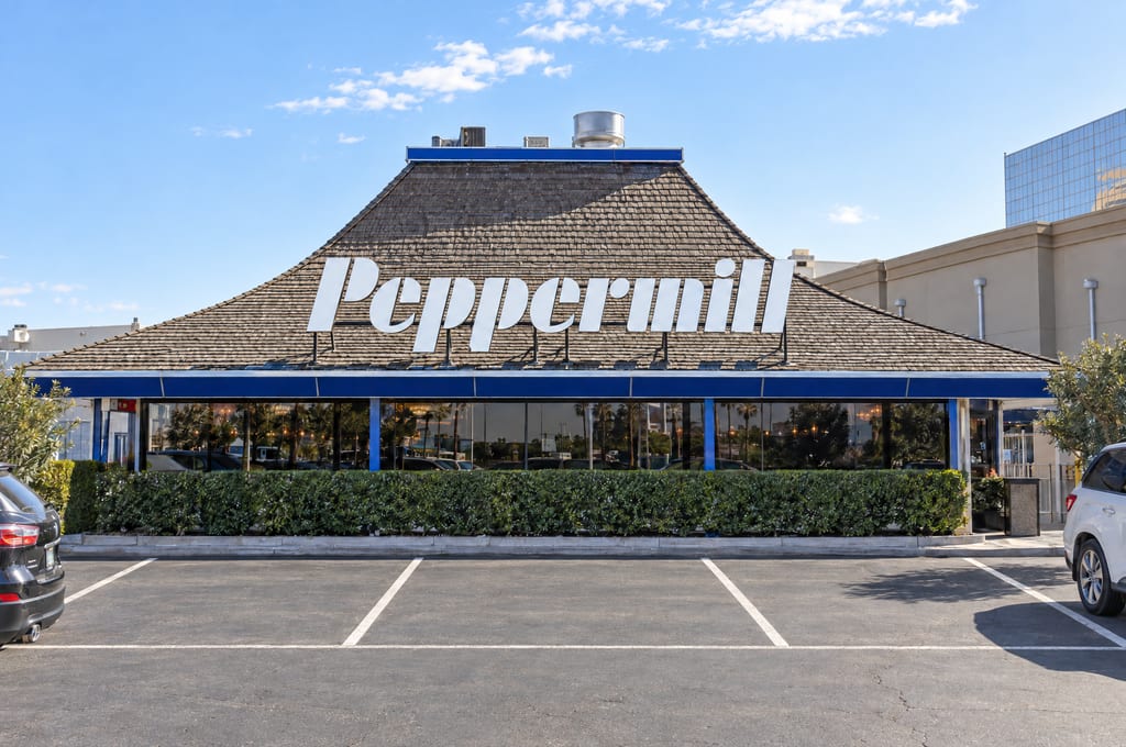 The Peppermill restaurant, its name in large white letters across a wood-shingled roof above a blue-trimmed band of windows, behind a clipped hedge and a row of empty parking spaces.