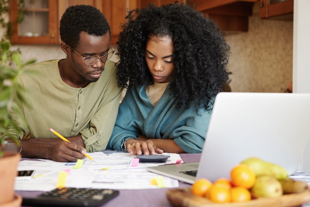 Two adults reviewing paperwork with a calculator and laptop at their kitchen table