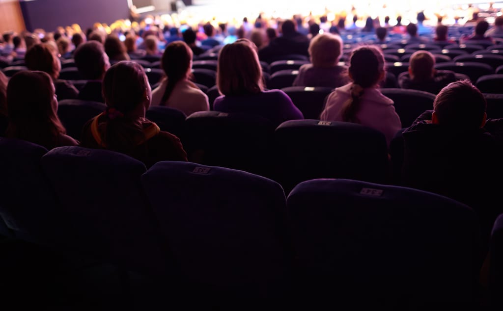 An audience seated in rows facing a brightly lit stage