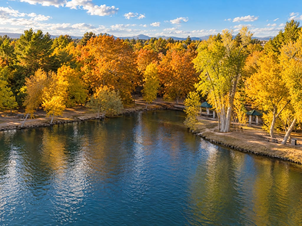 A park pond ringed by autumn trees, with picnic shelters on the bank and mountains far off