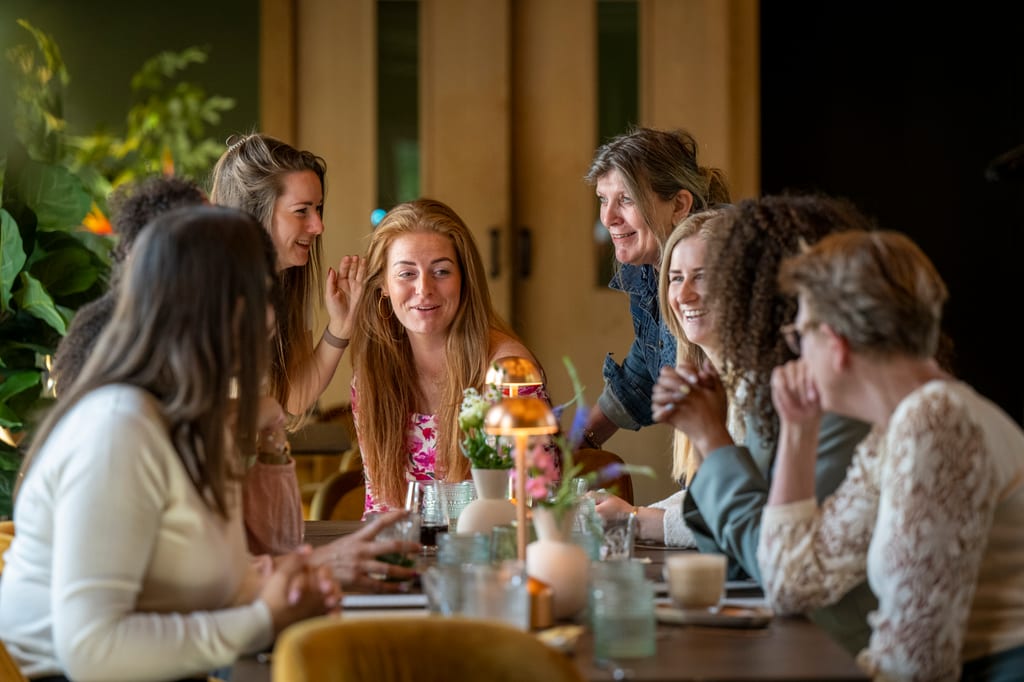 Friends talking around a restaurant table with flowers and soft table lighting.