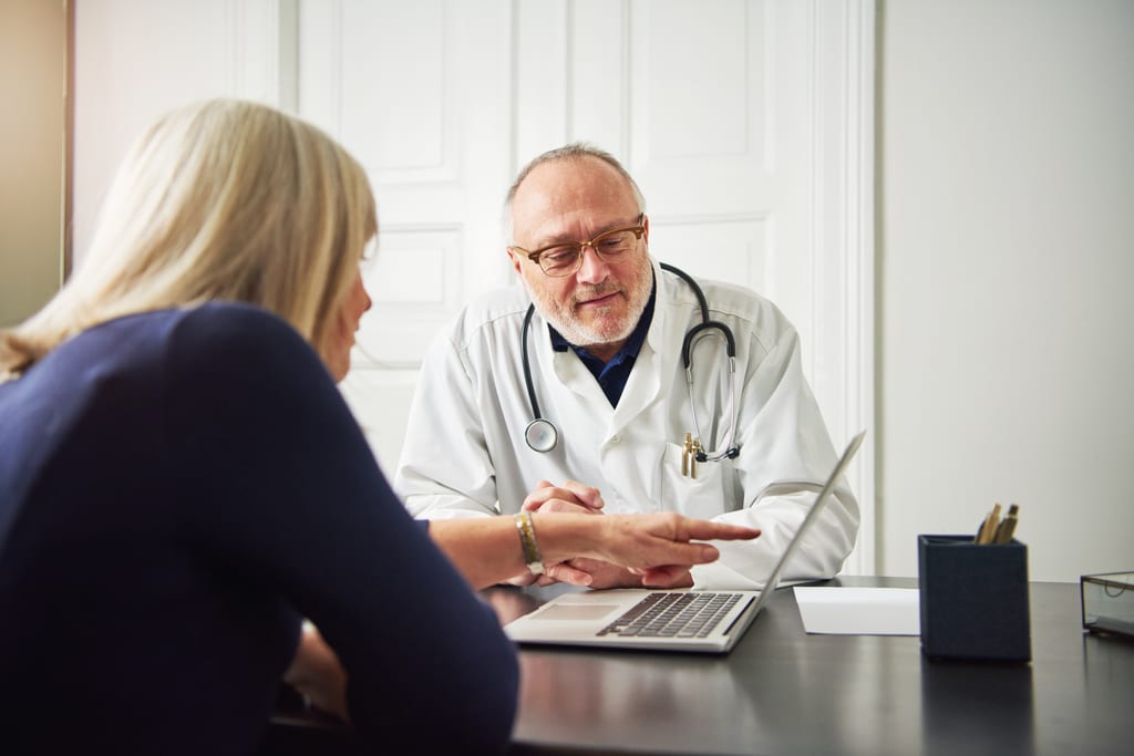 A patient and doctor discussing information on a laptop during an appointment.