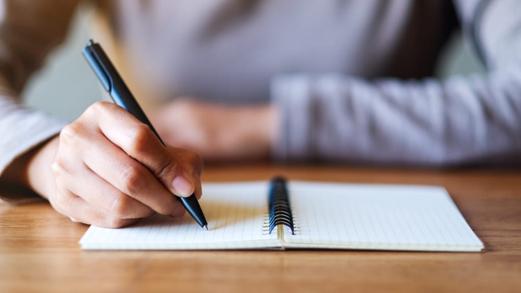 A hand holding a pen over an open notebook on a wooden table.