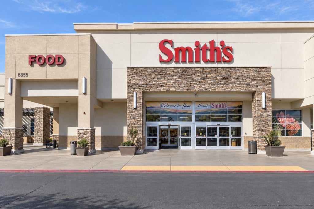 The entrance of a Smith’s store with the street number 6855, a stacked-stone archway over glass doors beneath a window banner reading Welcome to Your Aliante Smith’s.