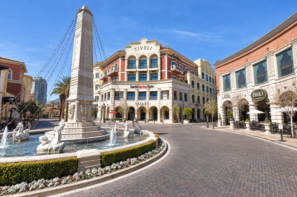 An obelisk fountain ringed with sea horse sculptures sits in a brick-paved roundabout in front of a red and cream building lettered Tivoli, with a Brio Italian Grille sign on the arcade to the right.